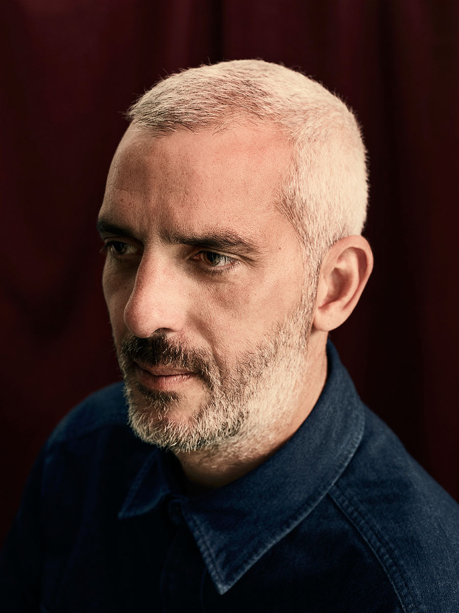 A head and shoulders portrait of Paul Rider, wearing a dark blue shirt against a dark background.