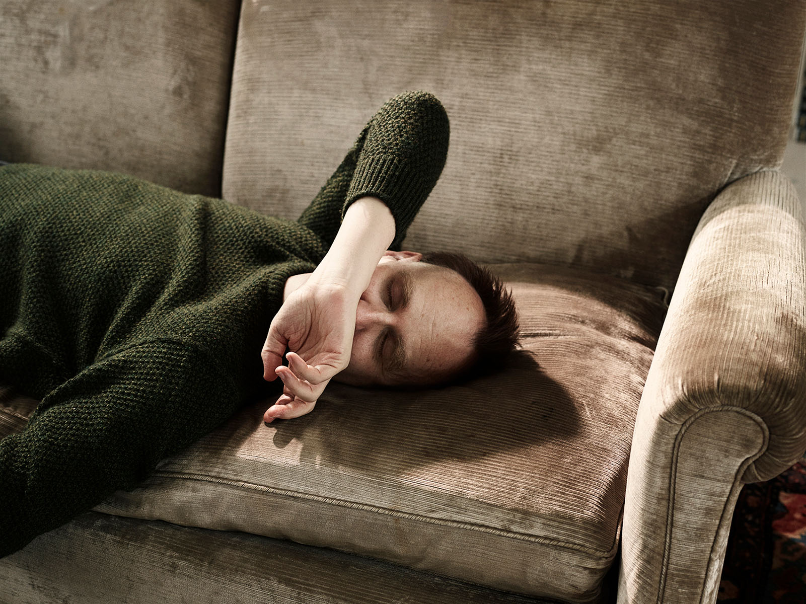 Photograph of Nick Harkaway lying supine on a couch with his hand across his face.