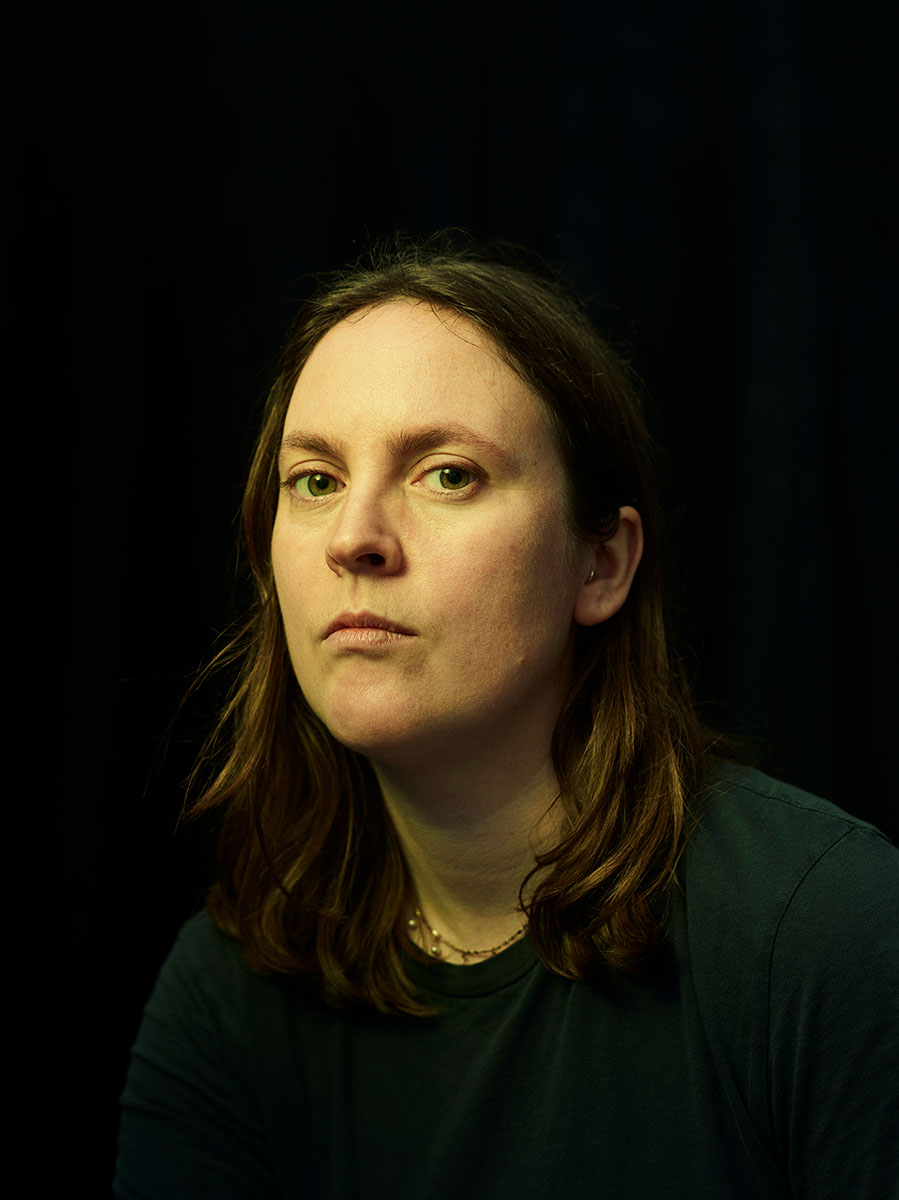 Studio portrait of painter, Maddie Yuille, against black background.